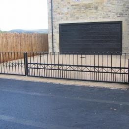 Double leaf wrought iron gates, with one on a track system and one on a swing arm